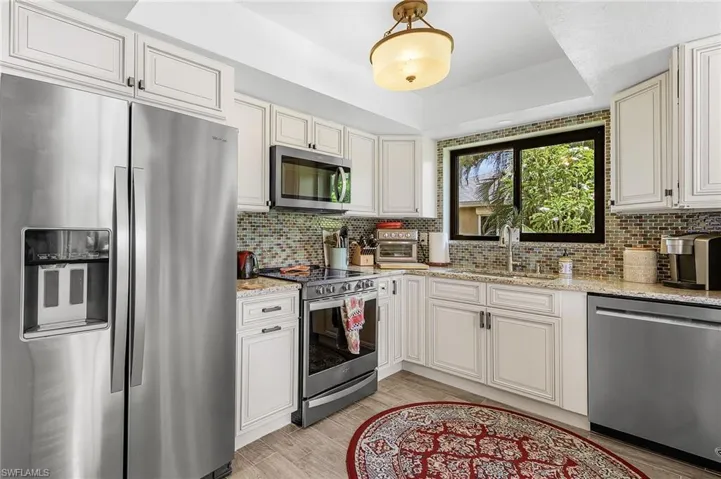 Kitchen featuring stainless steel appliances, light stone counters, light wood-style floors, decorative backsplash, and a raised ceiling