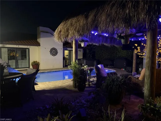 Pool at night featuring a patio, an outdoor pool, and a hot tub