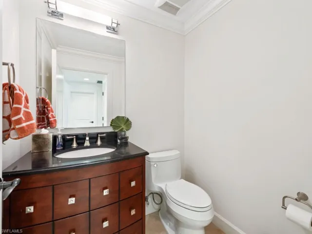 Half bathroom featuring visible vents, baseboards, ornamental molding, toilet, and vanity
