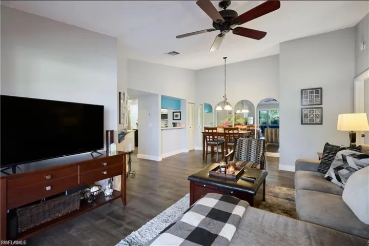 Living area featuring a chandelier, ceiling fan, baseboards, wood finished floors, and high vaulted ceiling