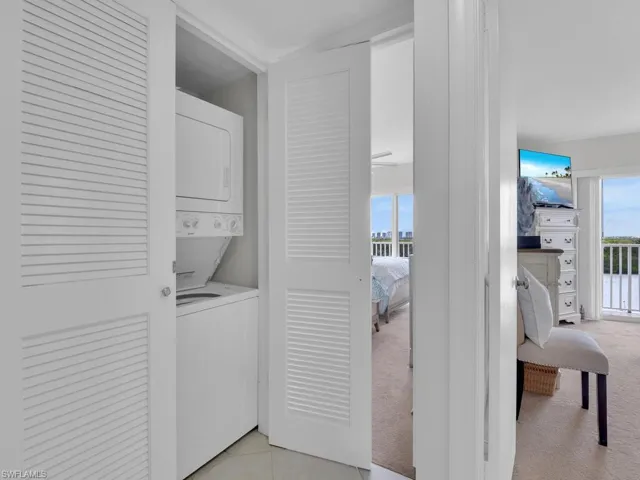 Laundry room with estacked washer and dryer, light carpet, and light tile patterned floors