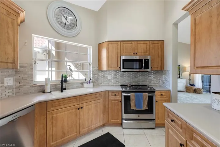 Kitchen with appliances with stainless steel finishes, light tile patterned floors, light countertops, decorative backsplash, and a towering ceiling