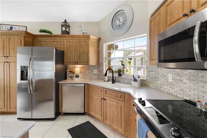 Kitchen featuring stainless steel appliances, light tile patterned floors, brown cabinetry, and backsplash