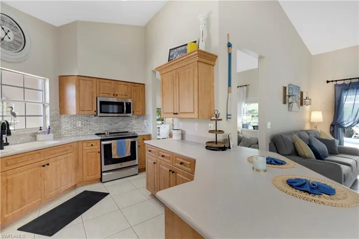 Kitchen with open floor plan, stainless steel appliances, light countertops, decorative backsplash, and high vaulted ceiling