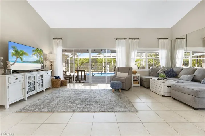 Living room with light tile patterned flooring, high vaulted ceiling, and a sunroom