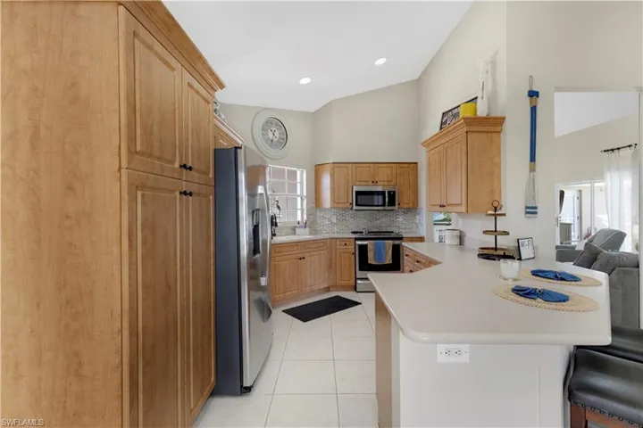 Kitchen featuring stainless steel appliances, tasteful backsplash, light tile patterned floors, light countertops, and a peninsula