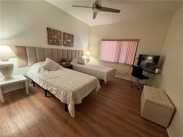 Vaulted ceiling bedroom featuring wood-finish flooring, a ceiling fan, and a window with vertical blinds