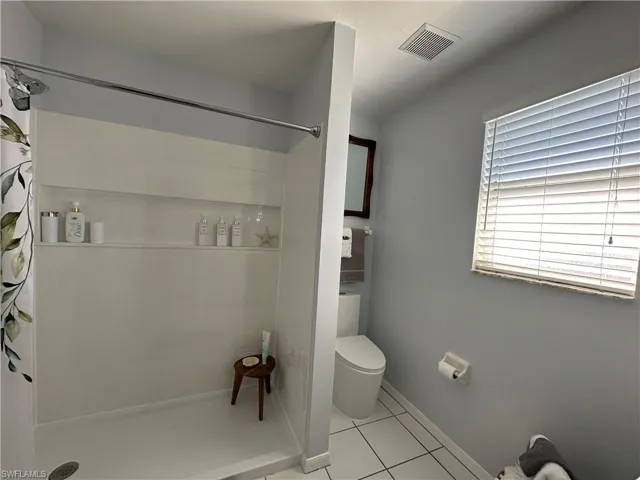 Bathroom with toilet, tile patterned floors, and a shower with curtain