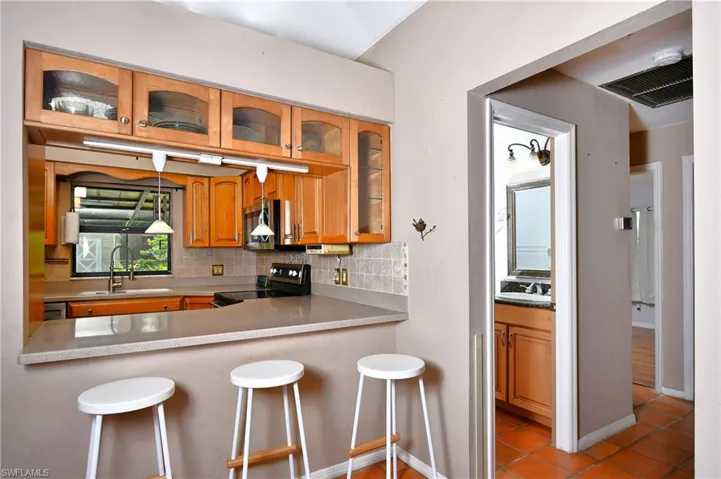 Kitchen featuring electric range, stainless steel microwave, decorative backsplash, light tile patterned floors, and a kitchen breakfast bar