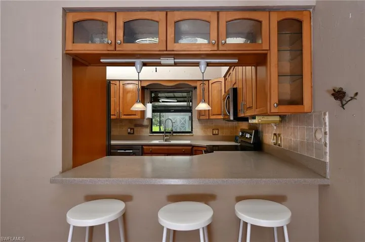 Kitchen featuring stainless steel appliances, brown cabinets, backsplash, glass insert cabinets, and a peninsula