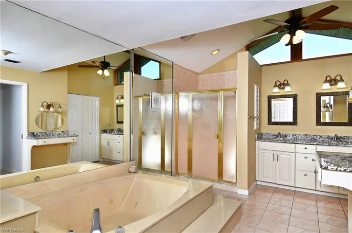 Master bathroom with a ceiling fan, vaulted ceiling, a stall shower, a whirlpool tub, and two vanities