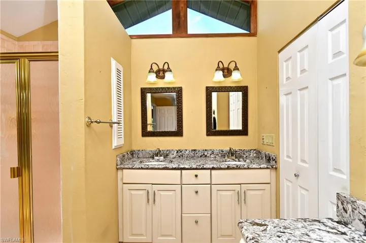 Bathroom with lofted ceiling, double vanity, a shower stall, and a closet