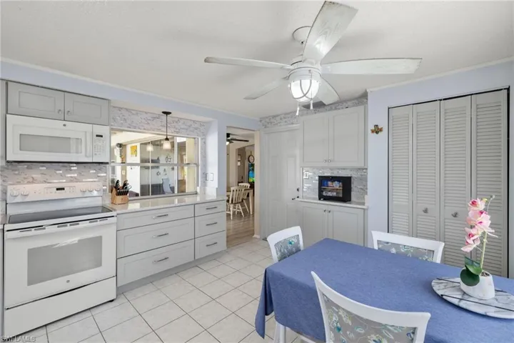 Kitchen with white appliances, light tile patterned floors, ceiling fan, backsplash, and decorative light fixtures