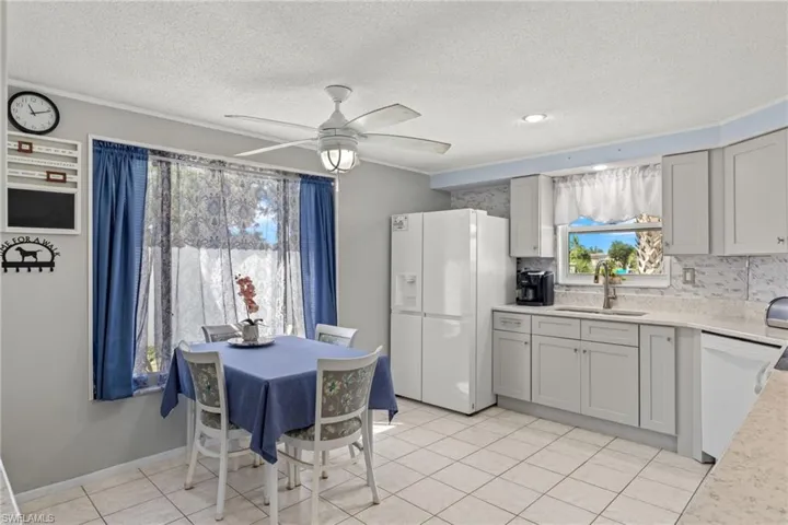 Kitchen with decorative backsplash, ceiling fan, light tile patterned floors, white appliances, and sink