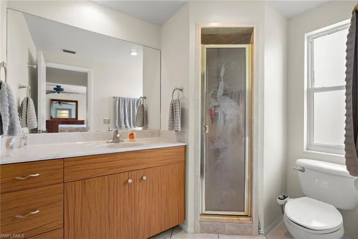 Primary Bathroom featuring a shower with shower door, a healthy amount of sunlight, toilet, and tile patterned flooring