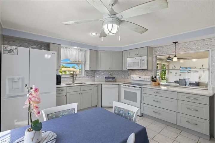 Kitchen with ceiling fan, sink, white appliances, and light tile patterned floors