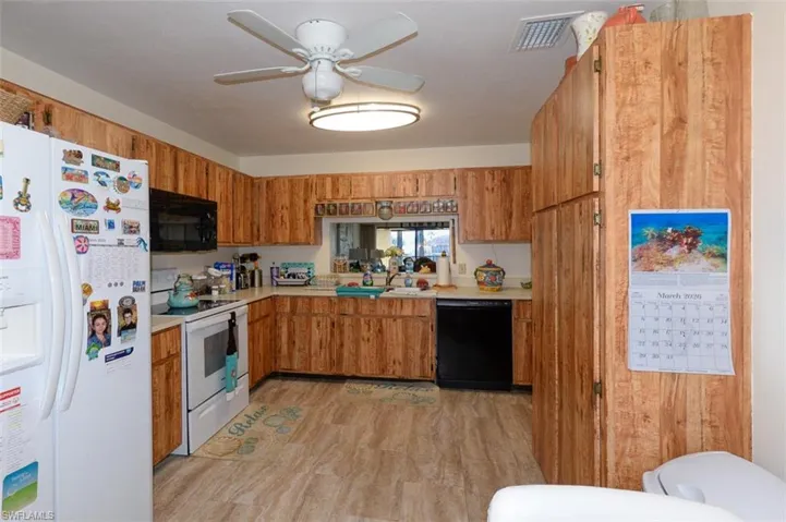 Kitchen with black appliances, light countertops, a ceiling fan, wood finish cabinets, and light wood-style floors