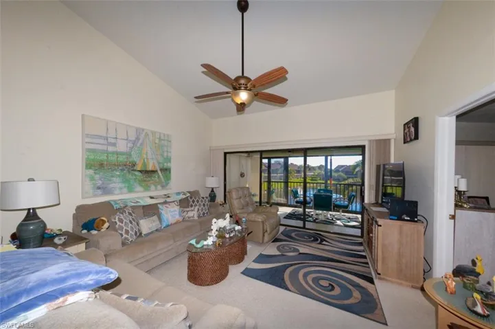 Living area with a ceiling fan, lofted ceiling, and light colored carpet