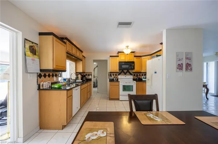 Kitchen featuring white appliances, decorative backsplash, dark countertops, and light tile patterned floors