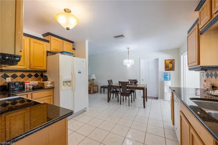 Kitchen featuring white appliances, decorative backsplash, and dark stone countertops