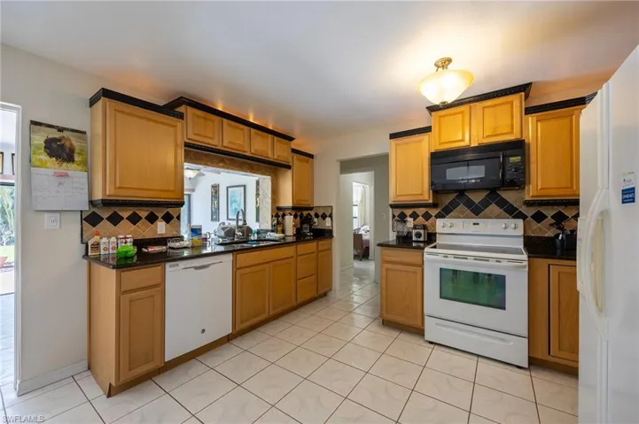 Kitchen featuring white appliances, tasteful backsplash, dark countertops, and light tile patterned floors