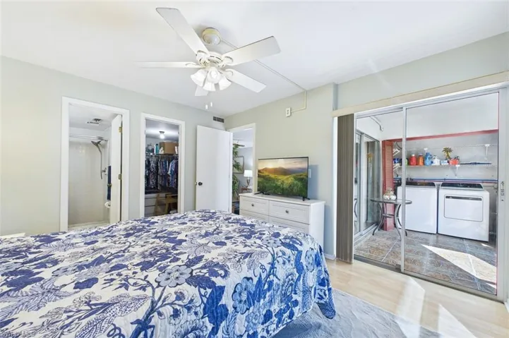 Bedroom with light wood-type flooring, a spacious closet, a ceiling fan, connected bathroom, and separate washer and dryer