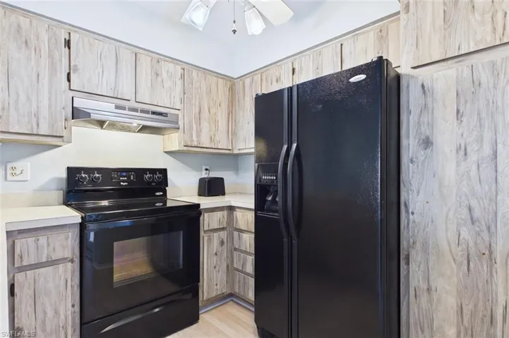 Kitchen with light wood finish cabinetry, black appliances, light countertops, and ceiling fan