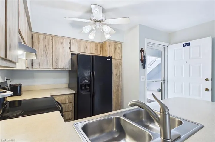 Kitchen with light countertops, black appliances, ceiling fan, and light wood finish cabinetry