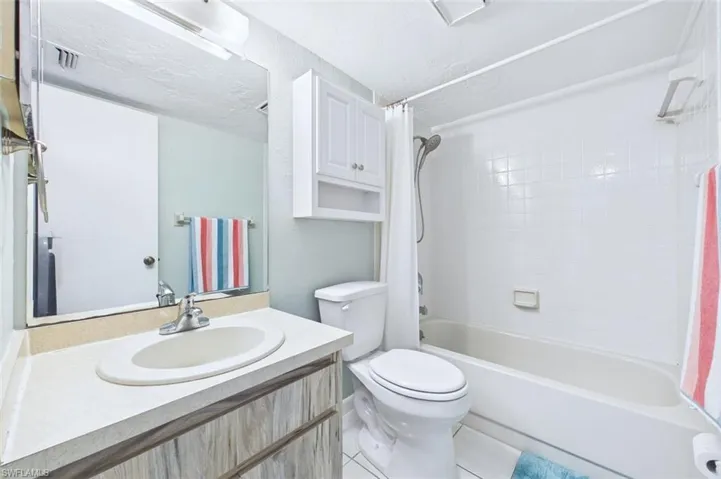 Full bath featuring vanity, shower / bath combo, light tile patterned floors, and a textured ceiling