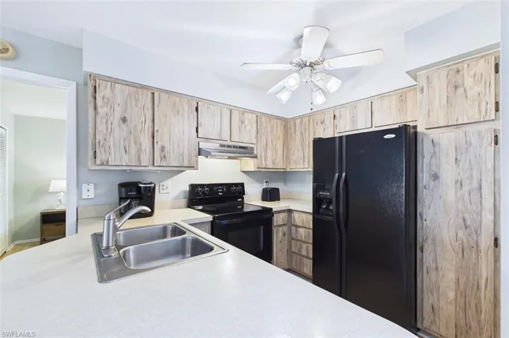 Kitchen featuring light countertops, black appliances, light wood finish cabinets, and a ceiling fan