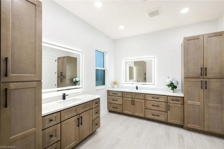 Full bathroom with two vanities, plank tile floors, recessed lighting, and dual  sink