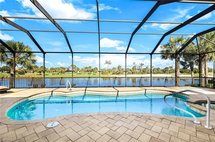 View of pool with glass enclosure, a pool with connected hot tub, a patio, and a water view