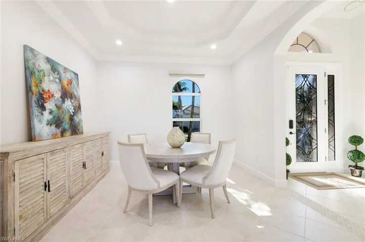 Dining room featuring a raised ceiling, ornamental molding, arched walkways, light tile patterned flooring, and baseboards