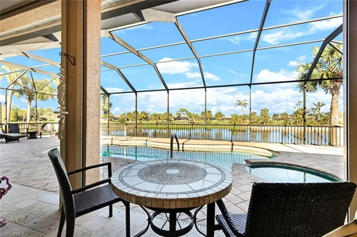 View of patio / terrace featuring a lanai, an outdoor pool, a water view, and an in ground hot tub and heated swimming pool