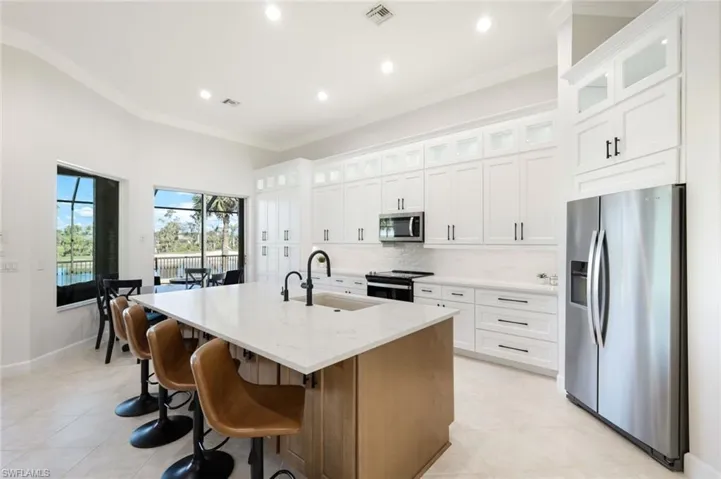 Kitchen featuring a sink, ornamental molding, decorative backsplash, stainless steel appliances, and a oversized kitchen island with sink