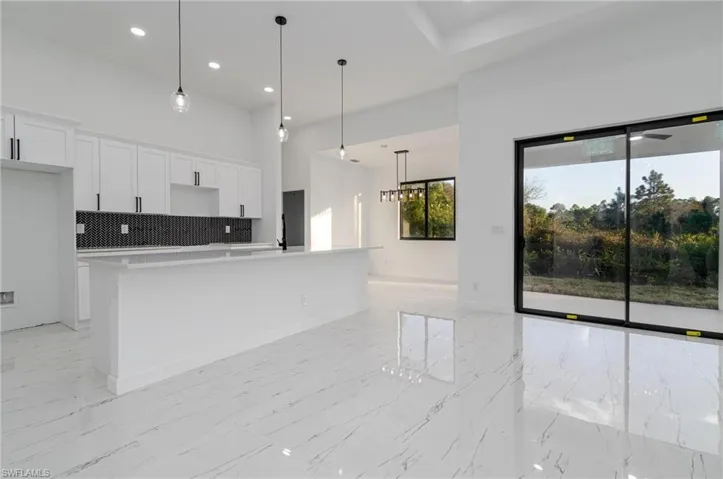 Kitchen featuring tasteful backsplash, white cabinetry, pendant lighting, and an island with sink