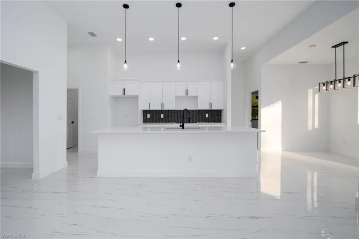 Kitchen with pendant lighting, sink, white cabinetry, a high ceiling, and a large island with sink