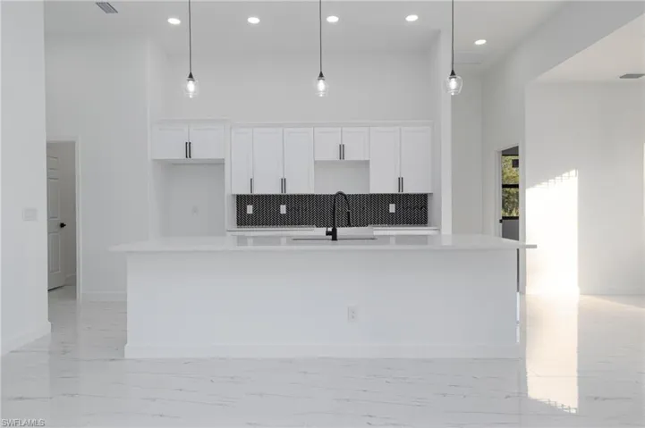 Kitchen with pendant lighting, white cabinetry, an island with sink, sink, and a high ceiling