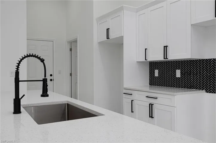 Kitchen with white cabinetry, light stone countertops, sink, and tasteful backsplash