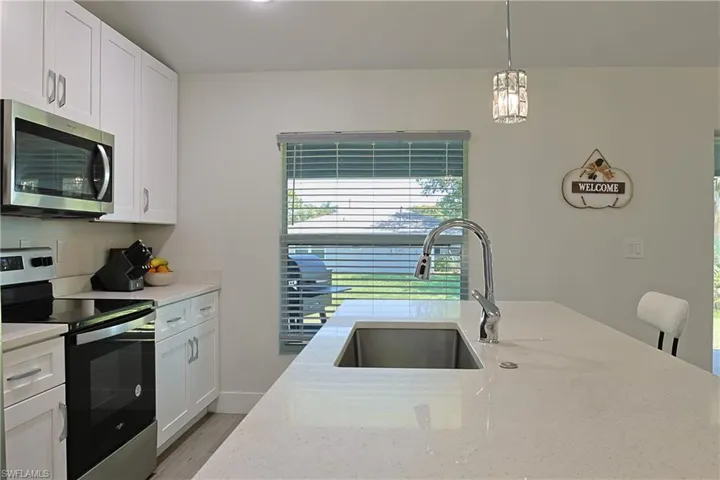 White shaker cabinetry with brushed nickel hardware, stainless steel appliances, a large island with an undermount stainless steel sink, a chrome high-arc faucet, and light-toned countertops