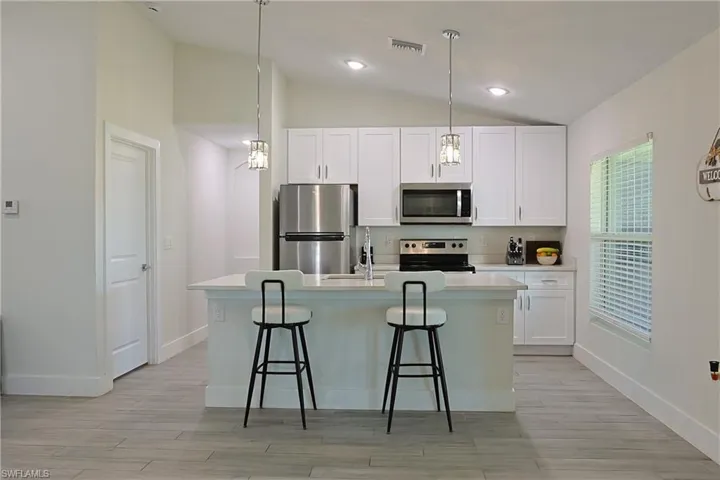 Kitchen featuring white shaker-style cabinetry, stainless steel appliances, a white island with pendant lighting, and wood-finish flooring