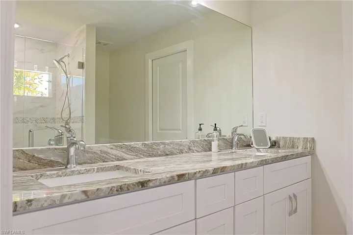 Dual vanity with stone countertop, undermount sinks, chrome faucets, and white shaker-style cabinetry