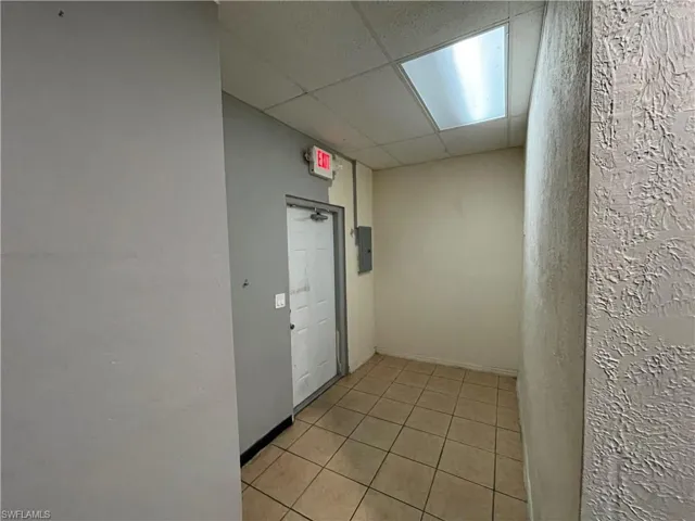 Hall featuring light tile patterned floors, a drop ceiling, and electric panel