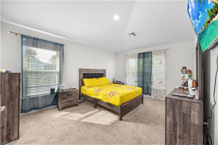 Recessed lighting, wood-finish headboard, window with blinds, carpeted flooring, two windows with curtain rods