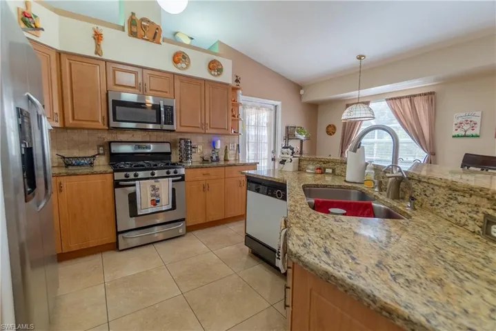 Kitchen with light tile patterned flooring, stainless steel appliances, lofted ceiling, a sink, and a wealth of natural light