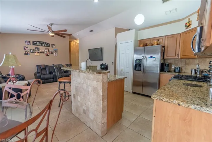 Kitchen with light tile patterned flooring, a ceiling fan, open floor plan, lofted ceiling, and stainless steel refrigerator with ice dispenser