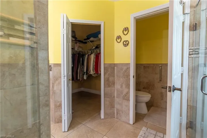 Full bath featuring tile walls, toilet, tile patterned floors, a stall shower, and a spacious closet
