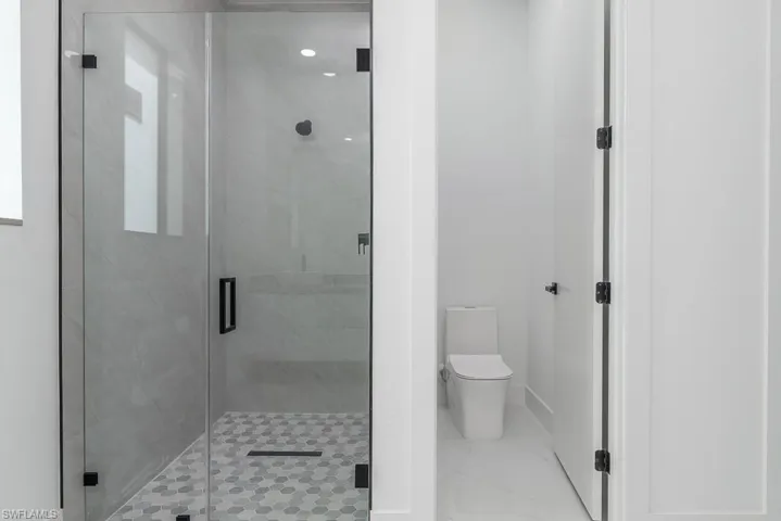 Full bath featuring a stall shower, marble finish floor, baseboards, and toilet