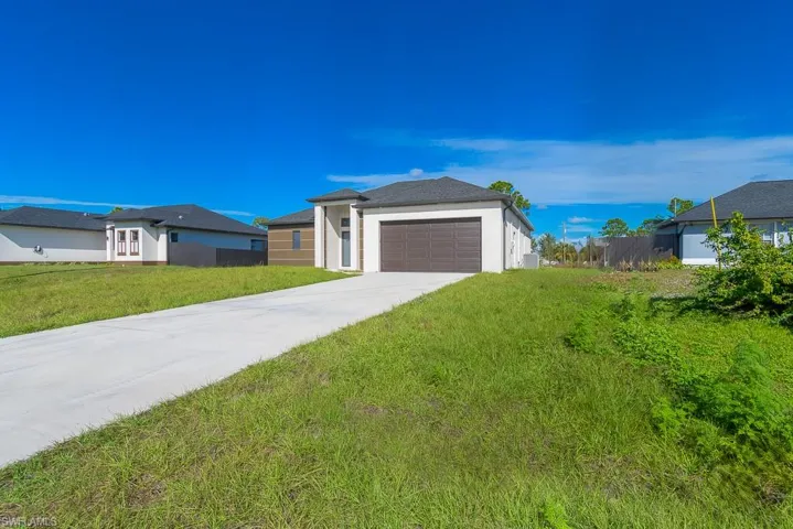 View of front of property featuring stucco siding, fence, a garage, driveway, and a front lawn