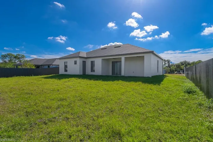 Back of property featuring fence, a lawn, and stucco siding